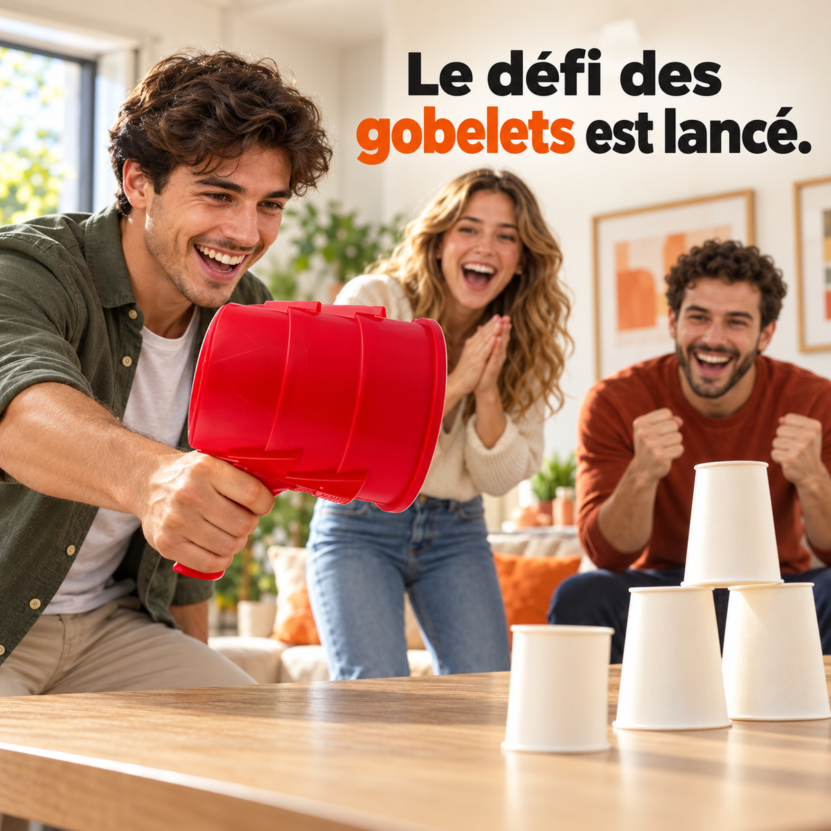 Défi des gobelets : un homme tient un canon à air vortex rouge devant des gobelets empilés, avec deux amis qui rient.